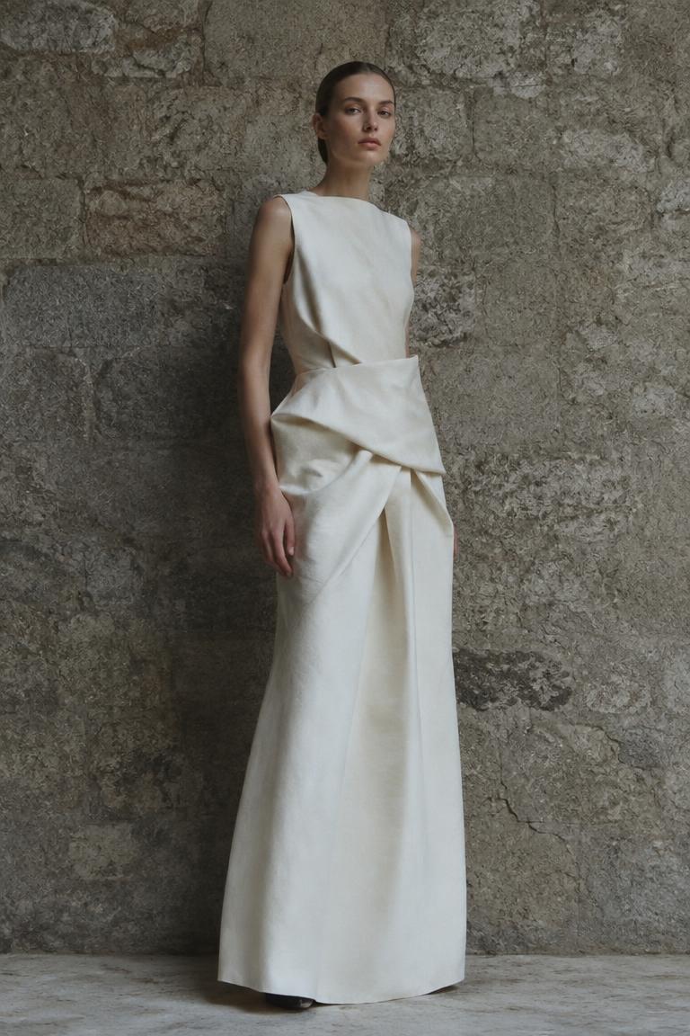 Model in a structured ivory silhouette dress against a stone wall
